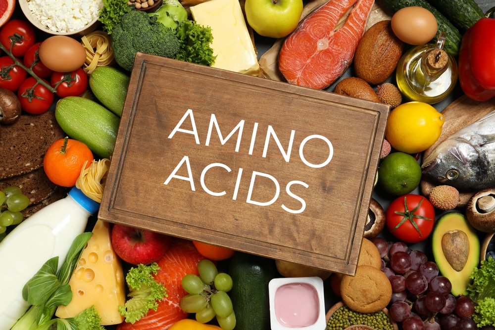 BCAAs vs. EAAs: Wooden board with text AMINO ACIDS among different products, top view
